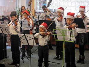 kids playing violin at event wearing santa hats