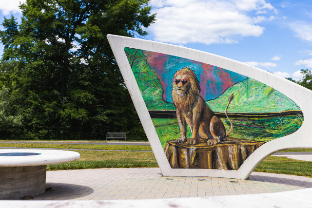 chalk drawing of a lion wearing heart-shaped sunglasses on an outdoor chalkboard in front of blue sky and trees